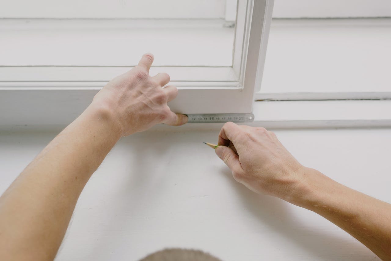 From above of crop unrecognizable male worker measuring window frame with metal ruler and pencil in house