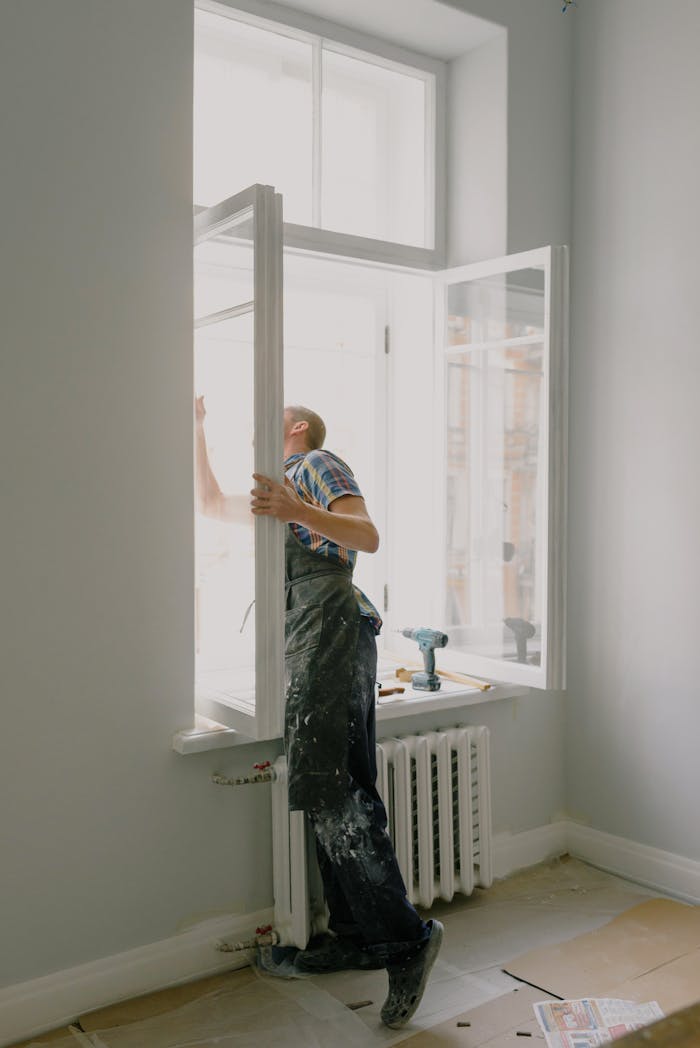 Side view of anonymous handyman in uniform mounting window frame during renovation process in flat
