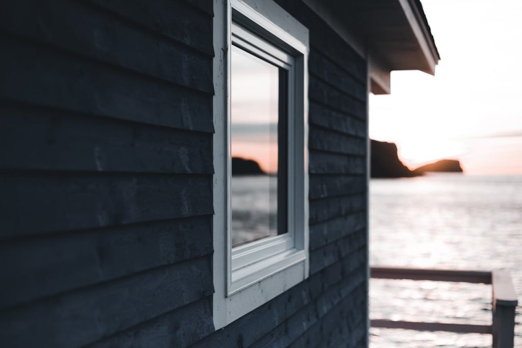 Wooden cabin by the sea capturing a serene sunset reflection in the window.