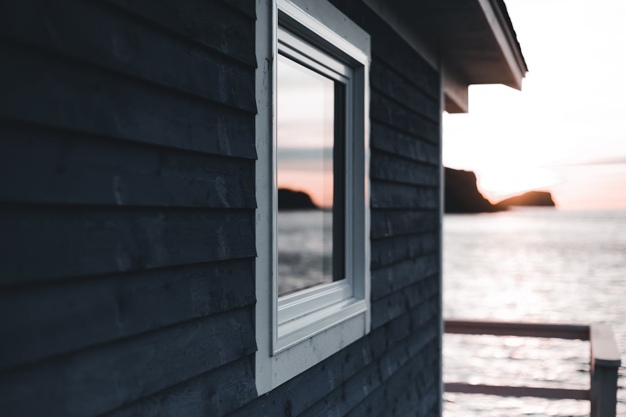 Wooden cabin by the sea capturing a serene sunset reflection in the window.