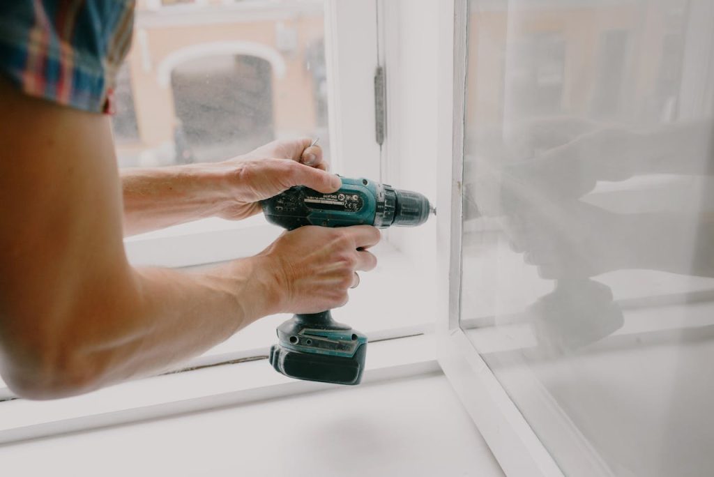 Side view of crop anonymous male mechanic fixing window with screwdriver during renovation process in apartment